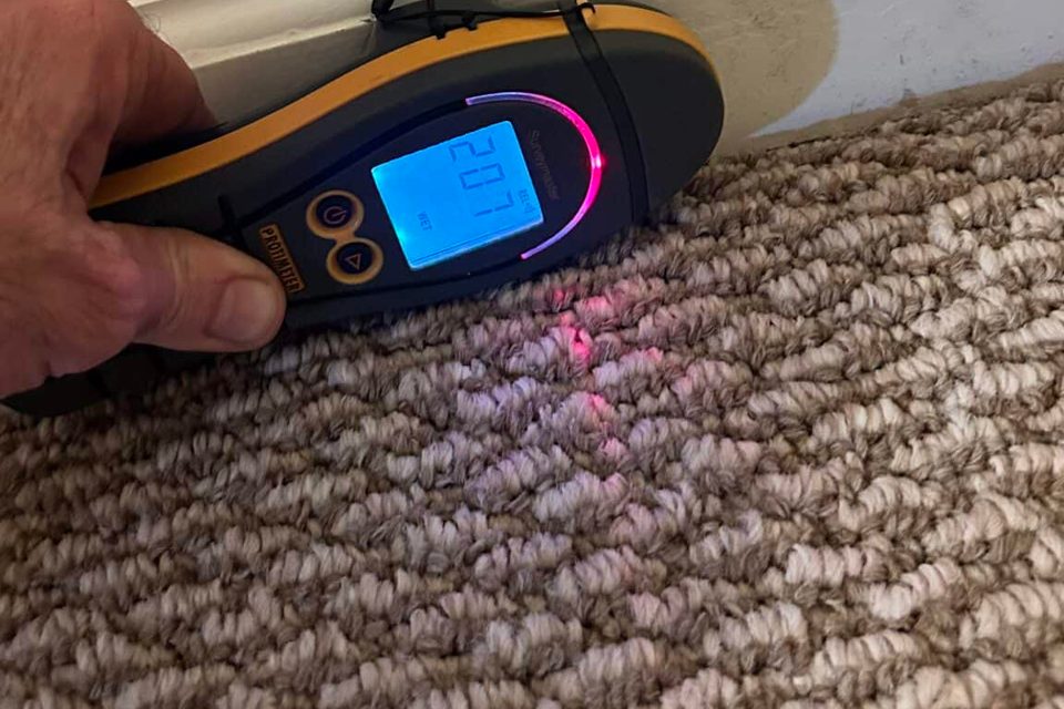 Handheld moisture meter beside removed baseboard
